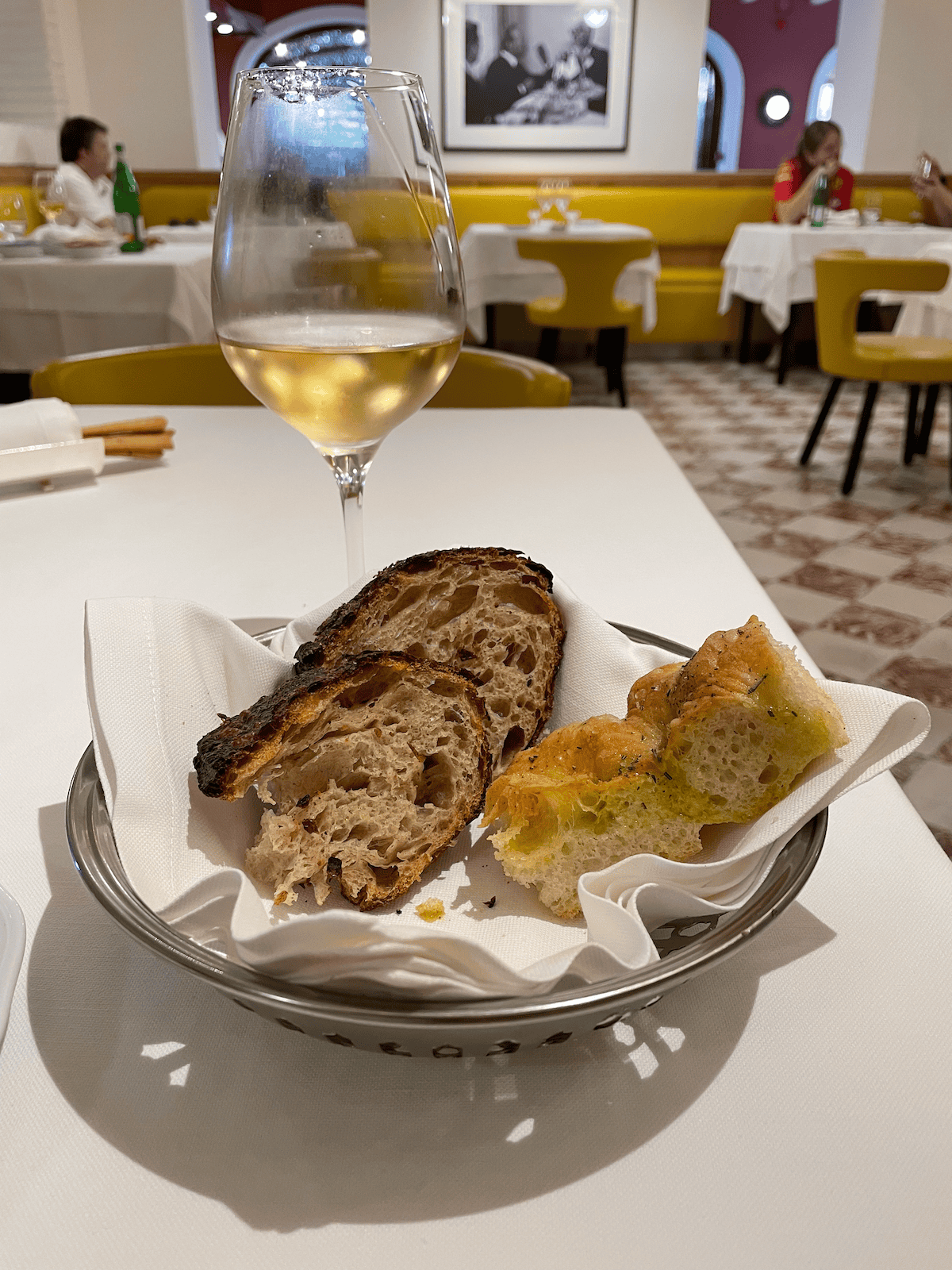a bread basket and a glass of red wine on a white linen-lined table at Ristorante Cavallino