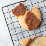 a tri-colored cookie in the shape of a cat on a black cooling rack